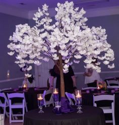 a table topped with a vase filled with white flowers and lit candles next to a tree