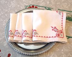 four white napkins on a silver plate with red and green designs in the middle