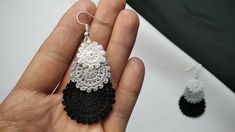 a hand holding a pair of black and white crocheted earrings