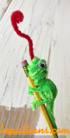 a green stuffed animal holding a yellow pencil