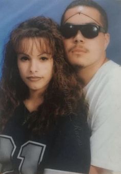 a man and woman posing for a photo in front of a blue background wearing sunglasses