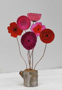 some paper flowers are in a vase on a white table and it looks like they have been made out of wood