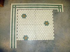 a tile floor with green and white flowers on it's border, in the middle of a room