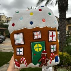 a hand holding up a gingerbread house ornament in front of a palm tree