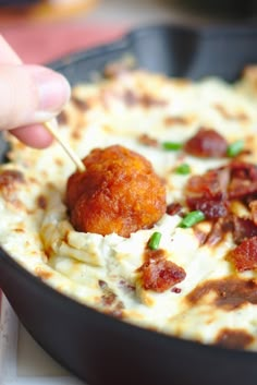 a person is dipping some food into a skillet with cheese and bacon on it