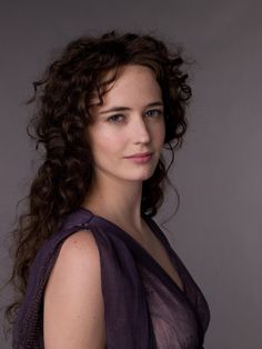 a woman with curly hair and blue eyes posing for a photo in a purple dress