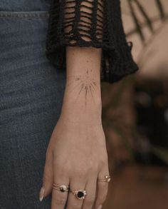 a woman's hand with a small sun tattoo on her left wrist and two rings