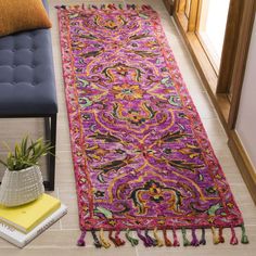 a colorful rug with tassels on the floor next to a blue chair and potted plant