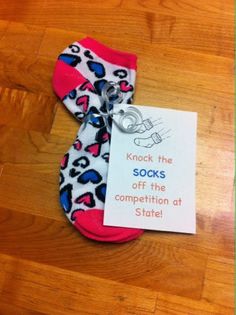 a sock with a tag attached to it sitting on a wooden floor next to a note that says knock the socks off the competition at state