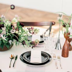 the table is set with black plates and silverware, flowers in vases, and place cards