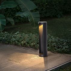 a lamp that is sitting on the ground near some bushes and trees in the background