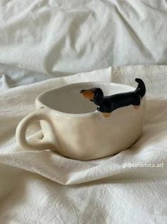 a small black and brown dog sitting in a cup on top of a white sheet