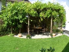 an outdoor dining area with table and chairs surrounded by greenery on the side of a house