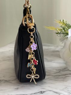 Dangly Purse Charm. A lovely chain style addition to dangle off your favorite purse. Other color choices are available for the charms, to customize your own unique design. Please message me if you are interested in more color options✨A cascade of multi color flower charms ending with a cute little rhinestone studded bow. Accessorize and elevate your bags look with this pretty accent for your purse or pochette. Purse Charm Care💕 ✨Use as an accessory for your bag and not a keychain, as it will maintain its beauty & longevity that way✨ ✨To keep your purse charm in its best condition: ✨Avoid water, sprays and oils ✨Metals fade naturally over time. Use a cloth with a little bit of lemon juice to polish and bring back shine!✨ Studding My Purse, Elegant Dangle Charms, Luxury Women's Logo Bag Charm, Luxury Logo Bag Charm, Luxury Designer Bags With Logo Charm, Luxury Bag Charm With Logo, Handbag Picture Charms, Coach Aestethic Bags, Luxury Designer Bag With Logo Charm