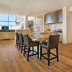 a kitchen with wooden floors and an island table surrounded by brown leather bar stools