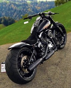 a black motorcycle parked on top of a dirt road next to a lush green hillside