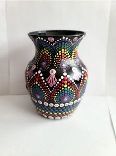 a black vase with multicolored designs on it's sides sitting on a white surface