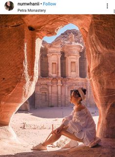 a woman sitting on the ground in front of a rock formation and looking out into the distance