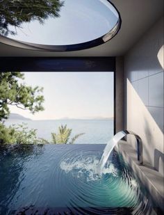 a pool with water coming out of it next to a large window that looks out onto the ocean