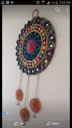 a colorful wall hanging on the side of a white wall with beads and chains attached to it