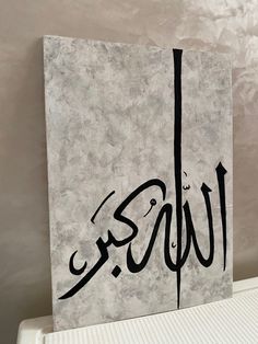 a piece of art with arabic writing on it sitting on top of a refrigerator freezer