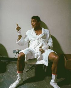 a man sitting in a chair with his hand up to the side while wearing white clothing