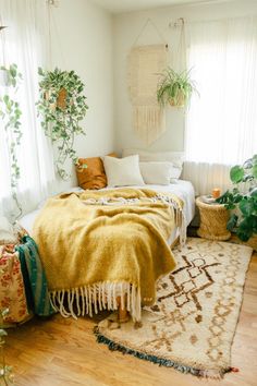 a bed with a blanket on top of it next to a window and potted plants