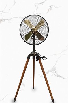 an old fashioned fan is on top of a tripod in front of a white marble wall