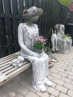 a statue sitting on top of a wooden bench next to flowers and potted plants