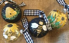 three glass ornaments with bees and sunflowers painted on them are sitting on a burlap surface