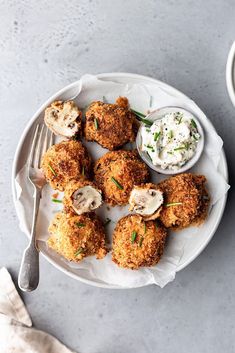 a white plate topped with fried food next to a bowl of ranch dressing and a fork