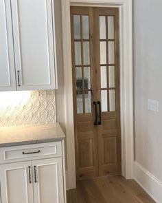 an empty kitchen with white cabinets and wooden doors, along with a wood flooring