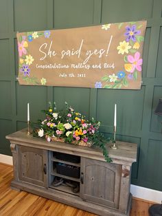 a wooden cabinet with flowers and candles on it in front of a sign that says she said get