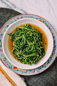 a white bowl filled with green vegetables on top of a table next to chopsticks