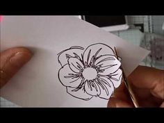 a person holding a piece of paper with a flower drawn on it next to a pair of scissors