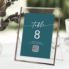 a table number sign sitting on top of a table next to a vase filled with flowers