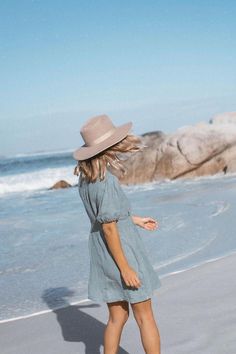 a woman walking on the beach wearing a hat