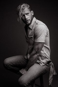 a man sitting on top of a stool wearing a shirt and jeans with his hands in his pockets