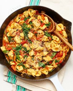 a skillet filled with pasta and spinach on top of a white table cloth