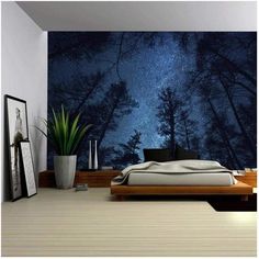 a bed room with a neatly made bed and a night sky wall mural behind it