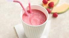 a smoothie in a paper cup with straws and raspberries on the side