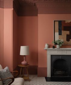 a living room with pink walls and a fireplace in the center, surrounded by two chairs