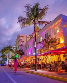 a woman walking down the street in front of a building with palm trees on both sides