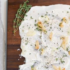 a wooden cutting board topped with lots of food on top of white sauce and herbs