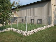 a fenced in area next to a building with grass and rocks on the ground