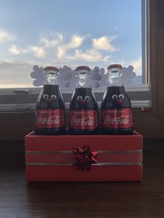 three coca - cola bottles are sitting in a red box with a bow on it