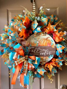 a fall wreath with an orange, blue and green bow hanging from it's front door