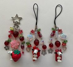 two pairs of earrings with charms attached to them on a white surface, one has a red strawberry and the other is a silver star