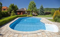 an empty swimming pool in the middle of a yard with trees and bushes around it