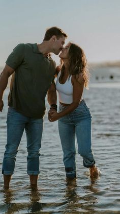 a man and woman standing in the water kissing each other with their noses close together